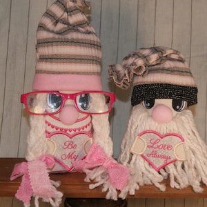 May include: Two Valentine's Day gnomes with pink and white hats, white beards, and pink hearts that say "Be My" and "Love Always".