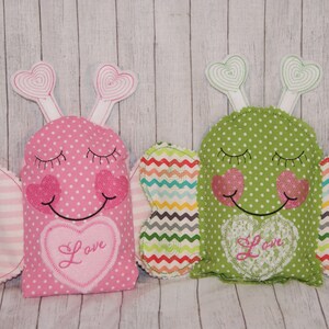 May include: Two plush butterfly-shaped pillows with embroidered eyes, smiles, and hearts. The pillows are pink and green with white polka dots and have the word "Love" embroidered on the front.
