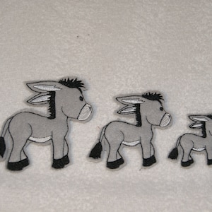 May include: Three gray donkey appliques in different sizes. The largest donkey is on the left, the medium donkey is in the middle, and the smallest donkey is on the right.