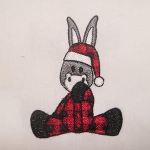 May include: Embroidered donkey wearing a Santa hat and red and black plaid pajamas. The donkey is gray with white accents and black hooves. The image is on a white background.