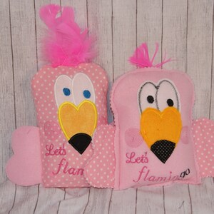May include: Two pink plush flamingo toys with embroidered eyes, beaks, and wings. The text "Let's flam" and "Let's flamingo" is embroidered on the front of each toy.