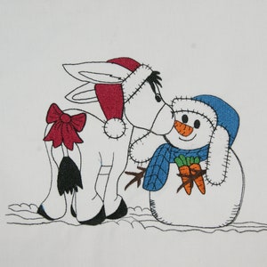 May include: A white donkey wearing a red Santa hat with a red bow on its tail is kissing a snowman wearing a blue hat and scarf. The snowman is holding two orange carrots.