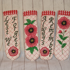 May include: Four red and white pot holders with embroidered poppies and the words "Lest We Forget" and "Always Remember".