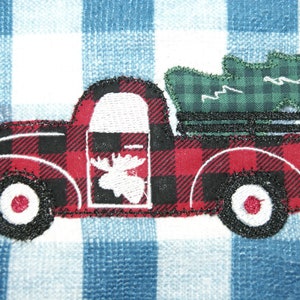 May include: Red and black plaid truck with a green plaid Christmas tree in the bed. The truck has a white moose on the side of the door.