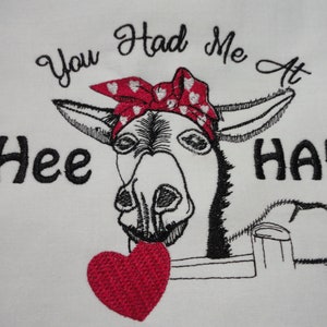 May include: Embroidered design of a donkey wearing a red bandana with white polka dots and holding a red heart. The text "You Had Me At Hee Haw" is embroidered above the donkey.