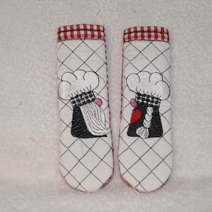May include: A pair of red and white checkered pot holders with embroidered images of chefs wearing hats. The chefs are wearing black and white checkered aprons and have white beards. One chef has a pink heart on their apron.