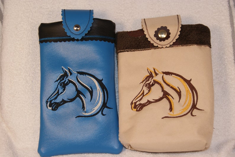 May include: Two phone cases with embroidered horse head designs. One case is blue with a white and black horse head, the other is beige with a brown and gold horse head.