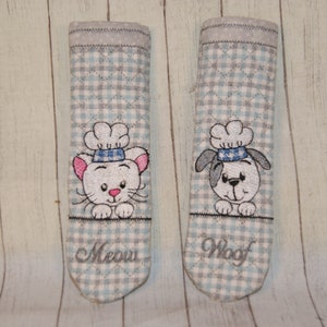 May include: Two gray and white checkered pot holders with embroidered animal faces. The left pot holder has a white cat with a chef's hat and the text "Meow". The right pot holder has a white dog with a chef's hat and the text "Woof".