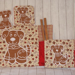 May include: Set of four brown and white quilted pot holders with embroidered dog designs. The pot holders feature a red and white checkered fabric on the back. The pot holders are decorated with hearts, bones, and paw prints.