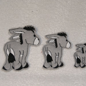 May include: Three grey felt donkey appliques in different sizes. The largest donkey is on the left, the medium donkey is in the middle, and the smallest donkey is on the right.