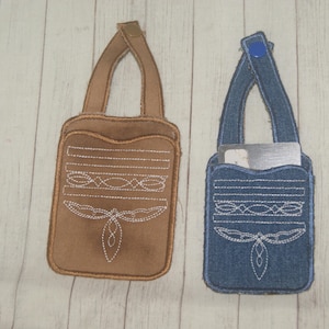 Könnte beinhalten: Zwei kleine, handgefertigte Taschen mit Henkeln. Eine ist braun, die andere jeansblau. Beide haben weiße Stickereien, darunter horizontale Linien und einen stilisierten Schmetterling. Die blaue Tasche enthält eine silberne Karte.