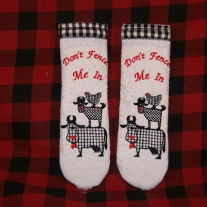 May include: A pair of white pot holders with black and white checkered trim. The pot holders have a black and white embroidered design of a cow, a sheep, and a chicken with the text "Don't Fence Me In".