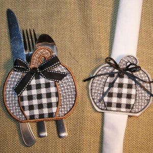May include: Two black and white checked pumpkin napkin rings. One ring is holding a set of cutlery, while the other is holding a white napkin.