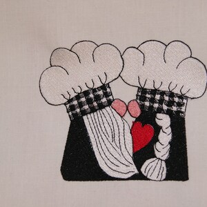 May include: Embroidered design of two chefs wearing white hats with black and white checkered bands, kissing with a red heart between them.