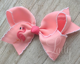 May include: A pink hair bow with a white scalloped edge and an embroidered flamingo design.