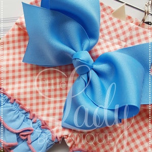 May include: A pink and white gingham fabric with a blue bow on top. The fabric has a ruffled edge and the bow is made of a satin ribbon.