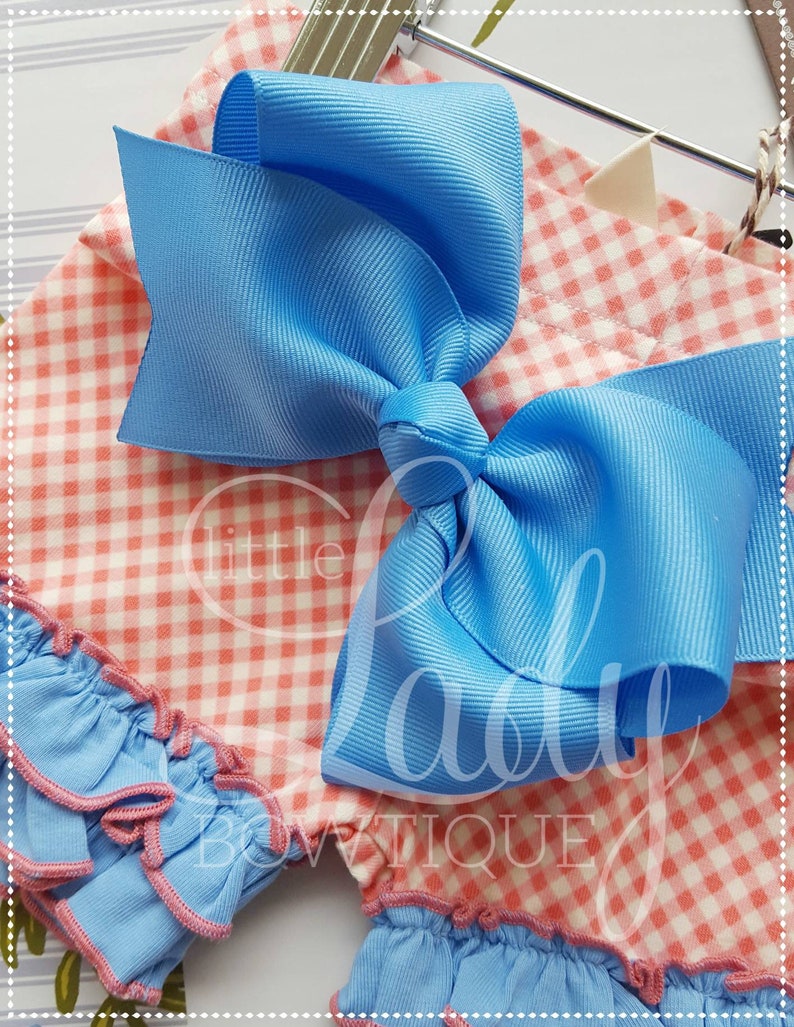 May include: A pink and white gingham fabric with a blue bow on top. The fabric has a ruffled edge and the bow is made of a satin ribbon.