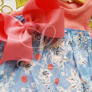 May include: A light blue and coral sleeveless dress with a white floral print and coral polka dots. A large coral bow is tied at the top of the dress.
