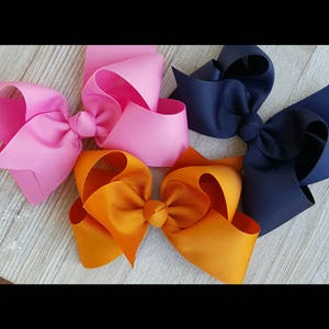 May include: Three hair bows in pink, orange, and navy blue. The bows are made of grosgrain ribbon and are tied in a classic bow shape.