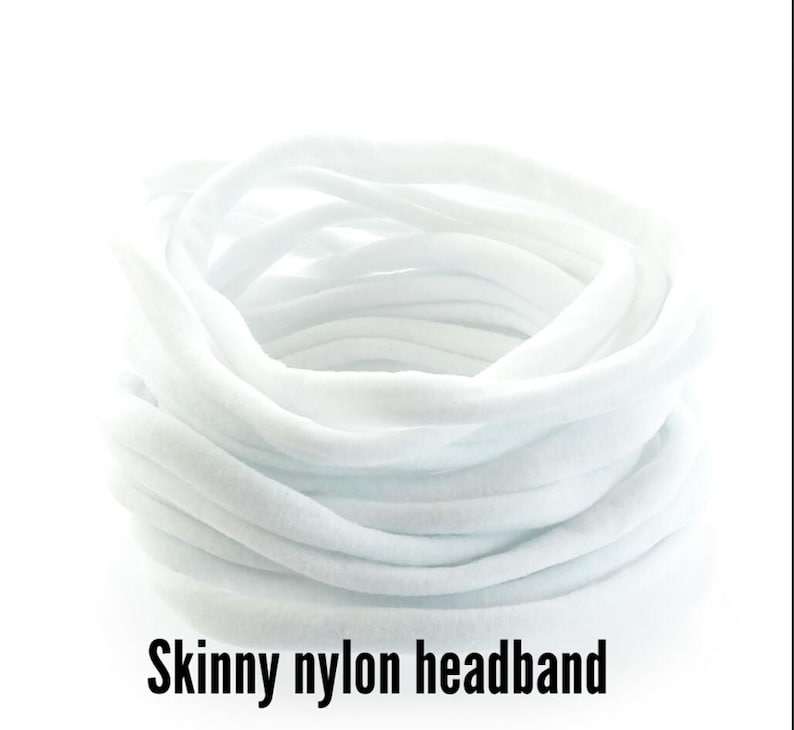 May include: A bundle of white, skinny nylon headbands. The headbands are tightly coiled, creating a circular shape. The text "Skinny nylon headband" is displayed in black at the bottom of the image. The headbands appear soft and flexible.