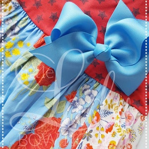 May include: A blue and white floral print dress with a red star print top and a large blue bow.
