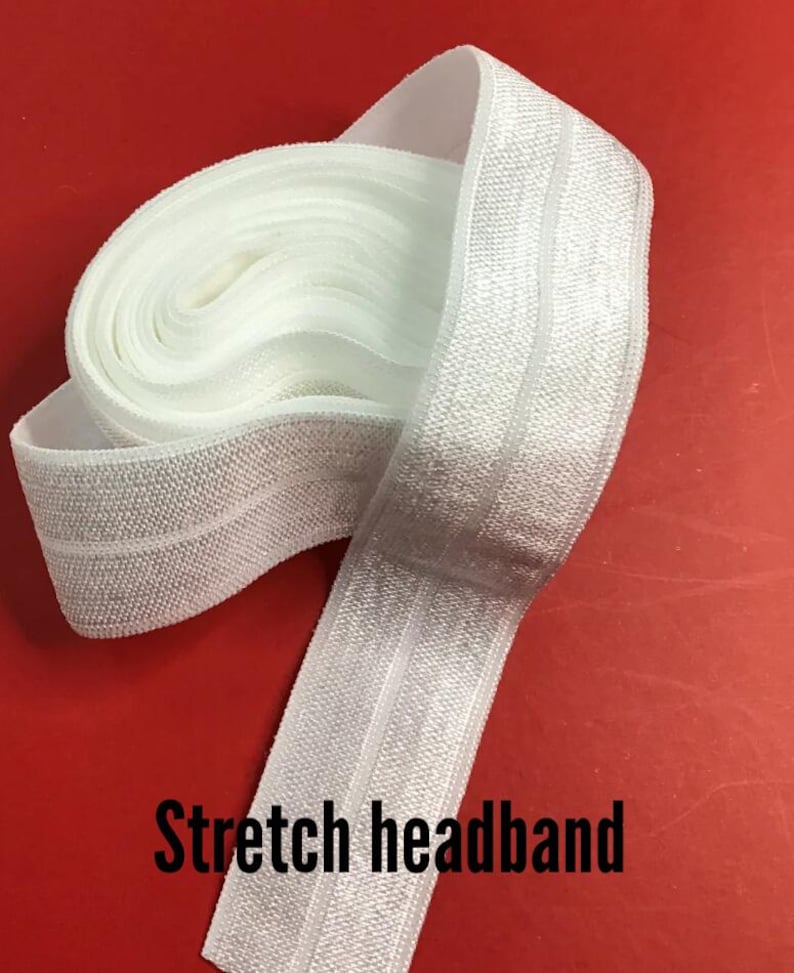 May include: White stretch headband, partially rolled, against a red background. The headband is made of a textured, elastic material. The text "Stretch headband" is printed in black at the bottom of the image.