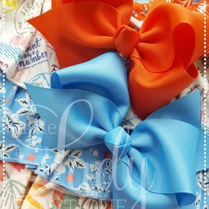 May include: Two hair bows, one orange and one light blue, are shown on a patterned fabric background. The bows are made of a grosgrain ribbon.