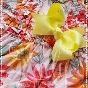 May include: A pink and white floral print dress with a yellow bow. The dress has a ruffled neckline and a floral pattern with orange, pink, and yellow flowers.
