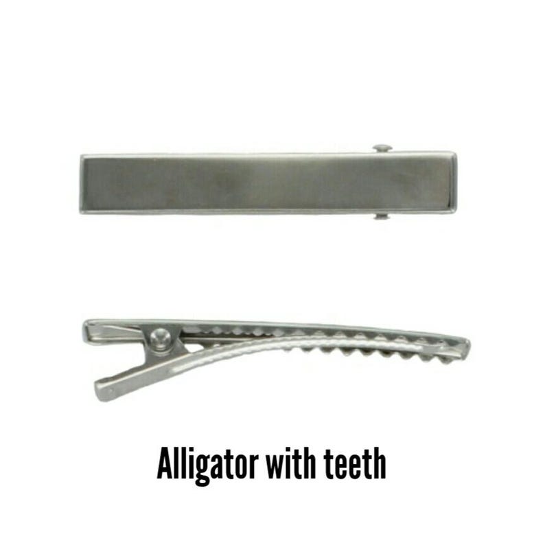 May include: Two silver-colored alligator hair clips. One clip is shown from the top, and the other is shown from the side, revealing the teeth. The text "Alligator with teeth" is below the clips.
