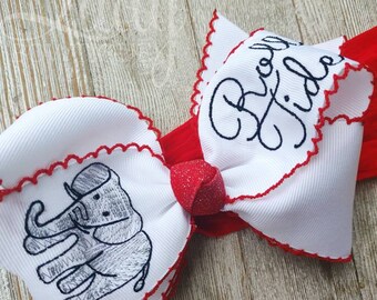 Può includere: Una fascia bianca e rossa con un grande fiocco. Il fiocco presenta un nastro bianco con un bordo smerlato rosso e un disegno di elefante ricamato. Le parole "Big Tide" sono ricamate sul fiocco.