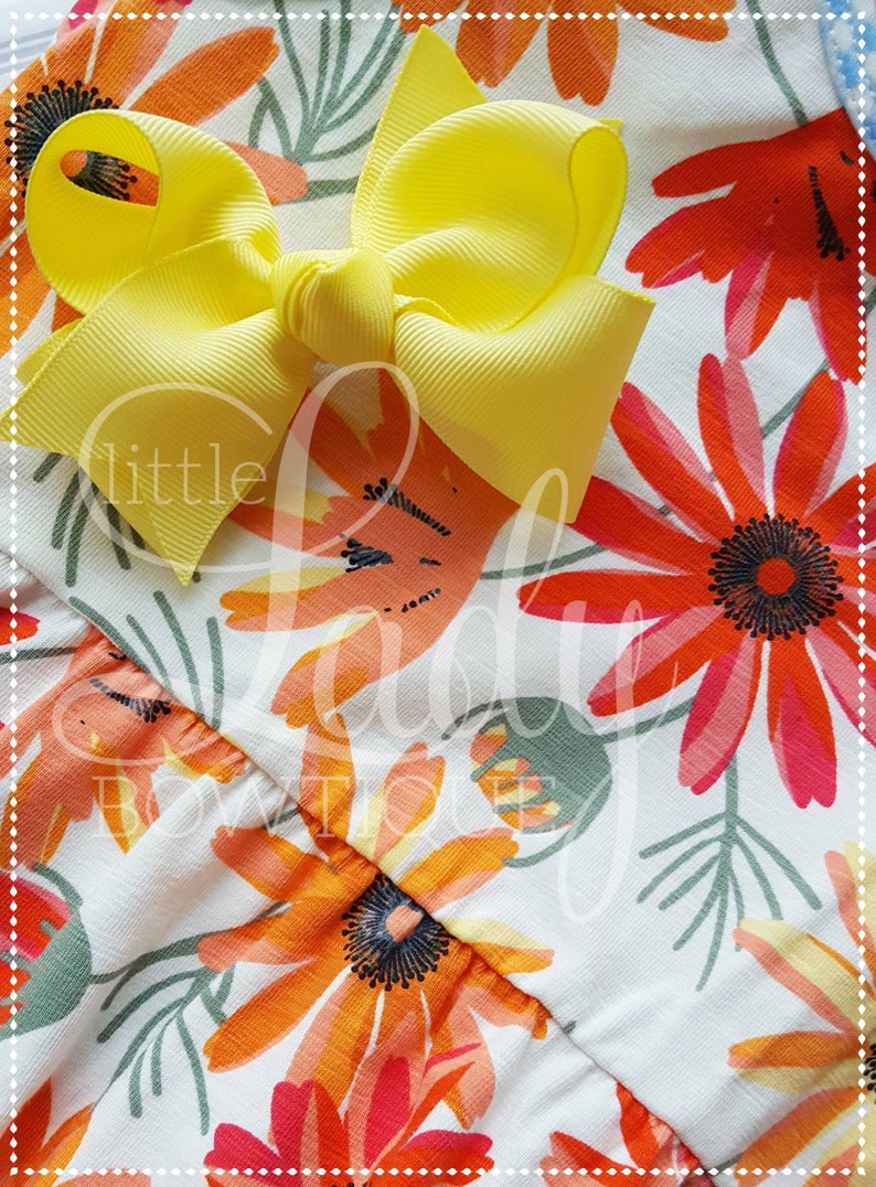 May include: A yellow bow with a white background featuring a floral pattern with orange, red, and green flowers. The text "little lady boutique" is visible in the image.