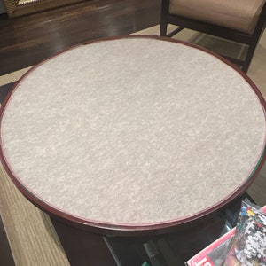 May include: A round wooden table with a light brown felt top. The table has a dark brown rim around the edge.