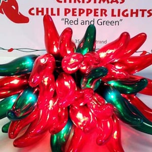 May include: Christmas chili pepper lights in red and green. The lights are shaped like chili peppers and are arranged in a cluster. The sign above the lights reads "Christmas Chili Pepper Lights".