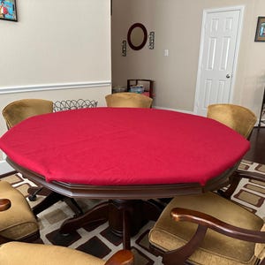 May include: A dark wood, octagonal dining table with a red tablecloth. The table is surrounded by six gold-colored upholstered chairs. The room has a neutral color palette with framed artwork and a patterned rug.