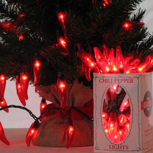 May include: Red chili pepper shaped Christmas lights strung on a green artificial Christmas tree. The lights are in a box that says "Chili Pepper Lights".