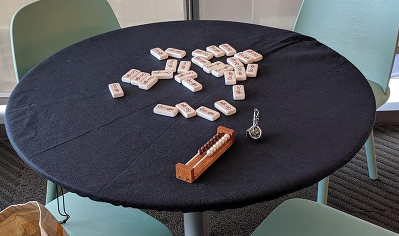 Puede incluir: Una mesa negra cubierta con un mantel negro con un juego de fichas de domin&oacute; blancas esparcidas sobre la superficie. Un peque&ntilde;o &aacute;baco de madera con cuentas marrones est&aacute; sobre la mesa, junto con un llavero plateado.
