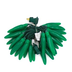May include: A bundle of green Christmas lights with a green cord and plug. The lights are shaped like elongated teardrops. The lights are on a white background.