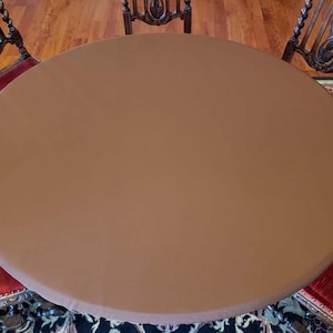 Puede incluir: Un mantel redondo marr&oacute;n que cubre una mesa con sillas. El mantel es liso y tiene una textura sutil.