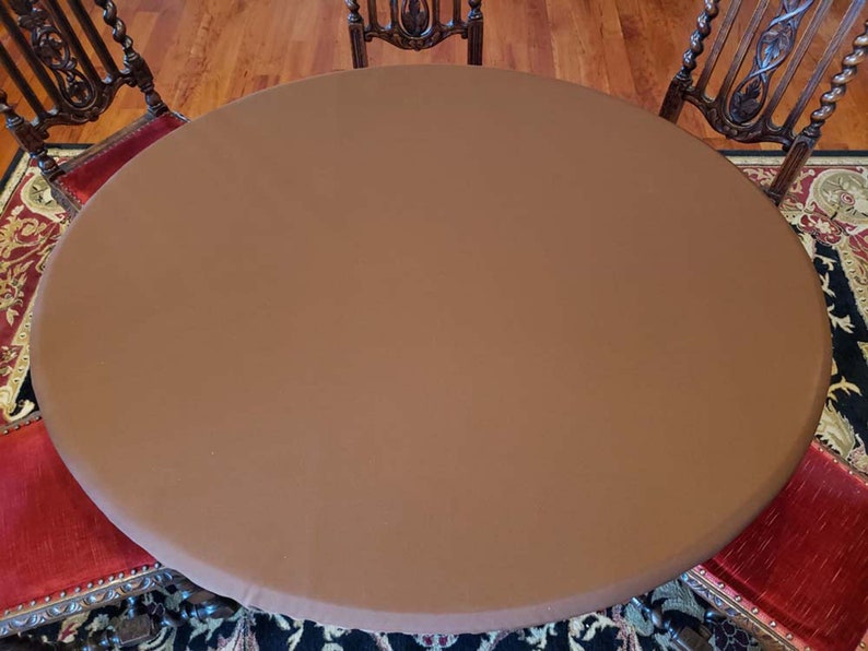 Puede incluir: Un mantel redondo marr&oacute;n que cubre una mesa con sillas. El mantel es liso y tiene una textura sutil.