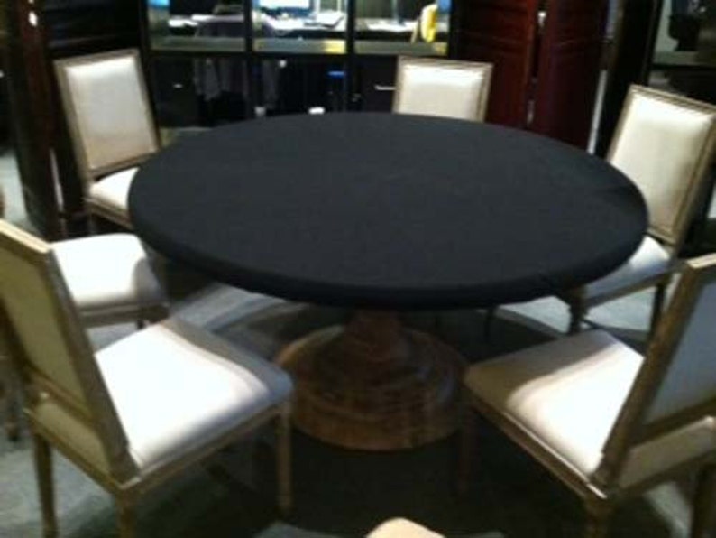 Puede incluir: Una mesa redonda con un mantel negro y seis sillas. Las sillas son de madera y tienen un asiento de tela blanca. La mesa est&aacute; en una habitaci&oacute;n con un suelo de madera oscura.