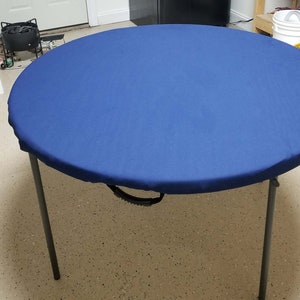 Puede incluir: Una cubierta de mesa redonda azul con un asa de transporte negra. La cubierta est&aacute; hecha de un tejido suave y duradero y es perfecta para proteger tu mesa de derrames y manchas.