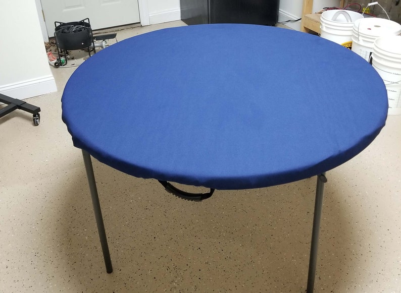 Puede incluir: Una cubierta de mesa redonda azul con un asa de transporte negra. La cubierta est&aacute; hecha de un tejido suave y duradero y es perfecta para proteger tu mesa de derrames y manchas.