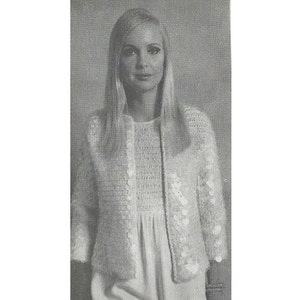 May include: A white crocheted cardigan with a button fastening and a floral design. The cardigan is cropped and has three-quarter sleeves.