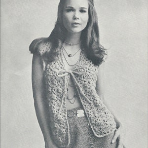 May include: A crocheted vest with a tie front and a delicate openwork pattern. The vest is worn over a patterned skirt and a layered necklace.