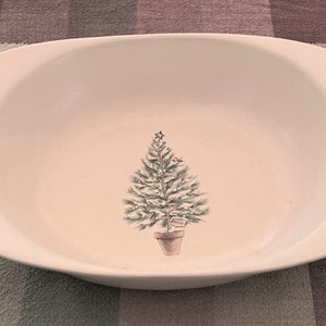 May include: White oval ceramic serving dish with green and white striped trim and gray handles. The dish features a hand-painted design of a green Christmas tree in a pot.