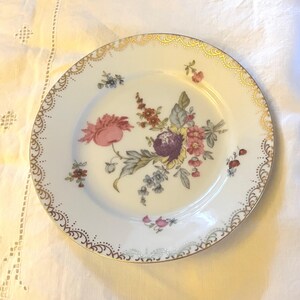 May include: A white porcelain plate with a gold rim and a floral design. The flowers are pink, purple, yellow, and blue.