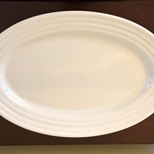 May include: A white, oval serving platter with a ridged rim. The platter is made of ceramic and is suitable for serving appetizers, entrees, or desserts. The clean design makes it a versatile piece for any dining occasion.