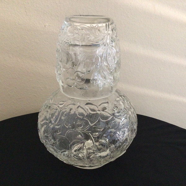 Jarra y taza de agua vintage de vidrio junto a la cama