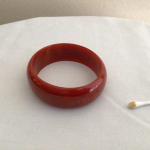 May include: A red plastic bangle bracelet. The bracelet is smooth and shiny.