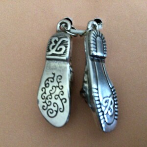 Pode incluir: Um par de pingentes de prata em forma de sapatos com desenhos florais intrincados.